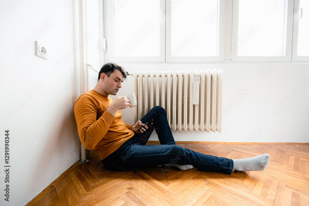 Man Sitting by Radiator Drinking Coffee in a Room With Wood Floor Man Sitting by Radiator Drinking Coffee in a Room With Wood Floor