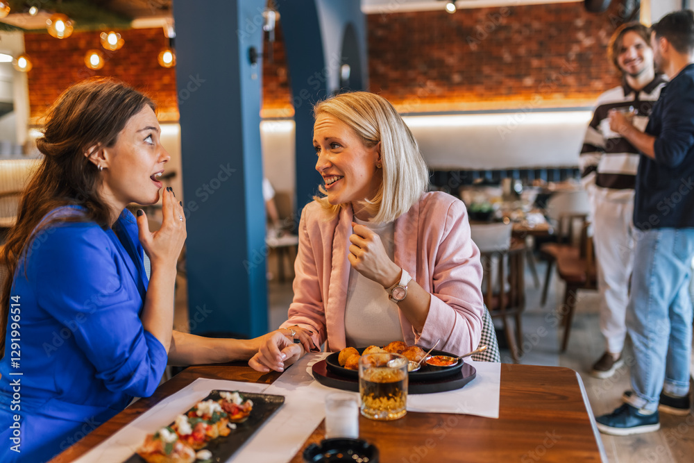 Fototapeta premium Two girl friends eating in a restaurant and they see cute boys behind them.