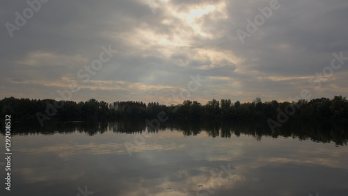 Lake with tree silhouettes reflecting in the water under a dark stormy sky in Damvallei nature reserve, Ghent, Flanders, Belgium  photo