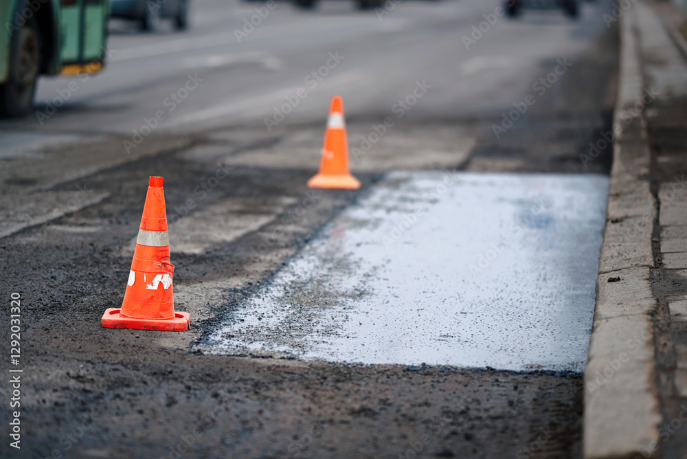 Pothole repair, traffic cones marking repaired asphalt section. Repairing pothole with fresh asphalt, traffic cones placed to separate construction area from moving vehicles for safety. Road repair
