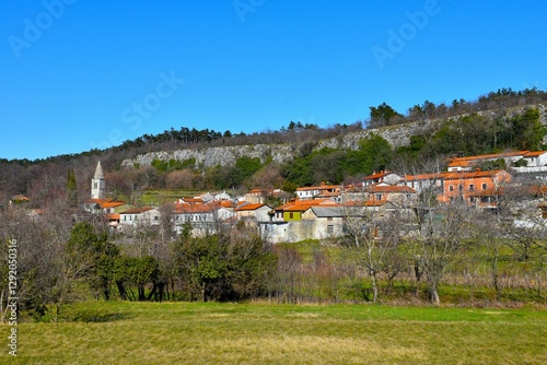 Wallpaper Mural View of Črnotiče village bellow a rock wall with the church tower and a meadow in front at Karst in Istria, Primorska, Slovenia Torontodigital.ca