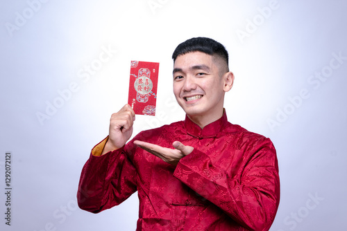 An Asian man in a red traditional Chinese Tang suit smiles while holding and presenting a single red envelope, symbolizing prosperity, isolated against a plain white background. photo