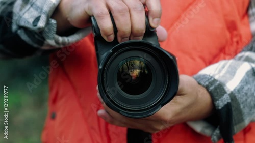 Professional photographer wearing bright orange vest, carefully adjusting camera settings while standing outdoors during photo shoot