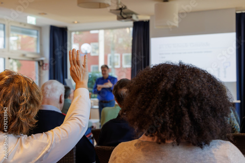 woman raising her hand during presentation of a male speaker between different age groups ans nationalities