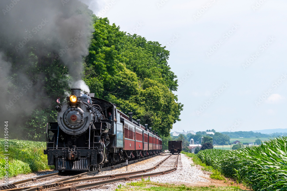 A steam locomotive puffs clouds of smoke as it glides along tracks in a vibrant green landscape. The sun shines brightly and fluffy clouds dot the blue sky, creating a picturesque scene. A steam locomotive puffs clouds of smoke as it glides along tracks in a vibrant green landscape. The sun shines brightly and fluffy clouds dot the blue sky, creating a picturesque scene.