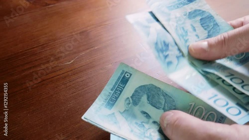 Close-up shot of a man's hand counting 100 Serbian dinar banknotes with the image of Nikola Tesla