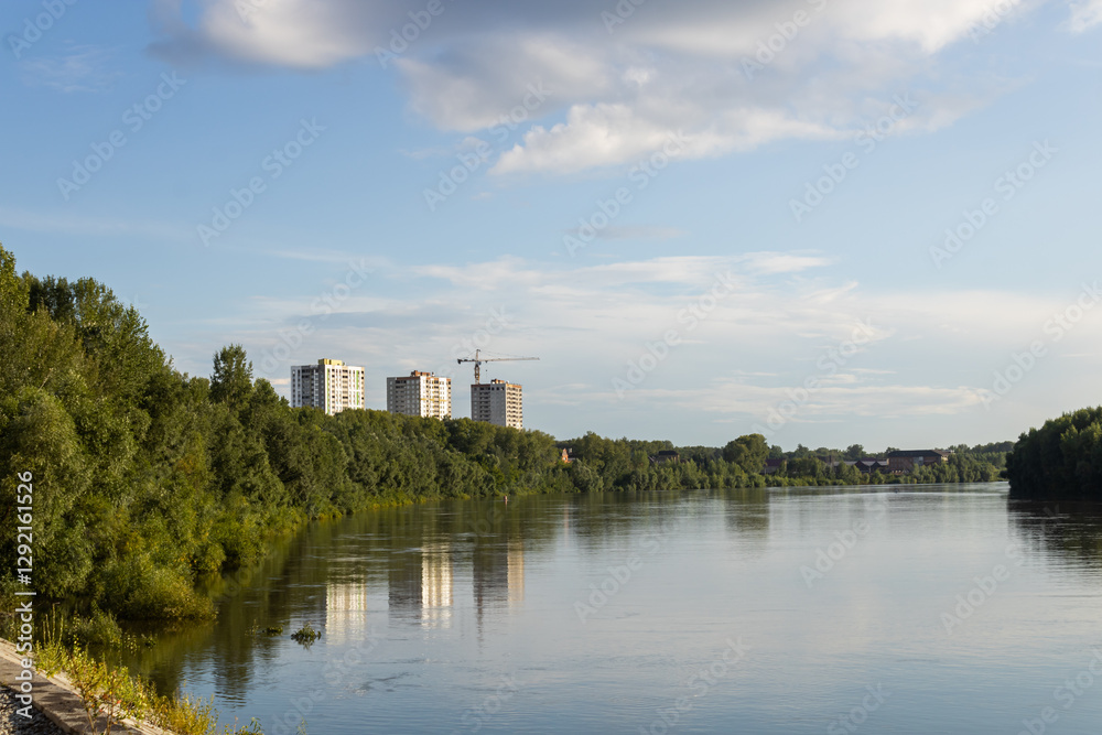 River, trees on the embankment, houses under construction and cranes. Cloudy sky on a sunny day. The capital of Bashkiria, the city of Ufa River, trees on the embankment, houses under construction and cranes. Cloudy sky on a sunny day. The capital of Bashkiria, the city of Ufa