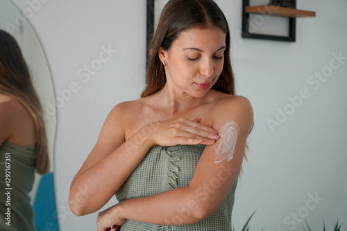 Relaxed beautiful young woman spreads body cream and takes care of her skin