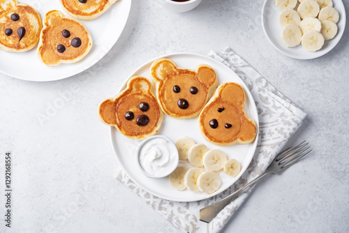 Pancakes in the form of bears with cream sauce and banana slices in a plate