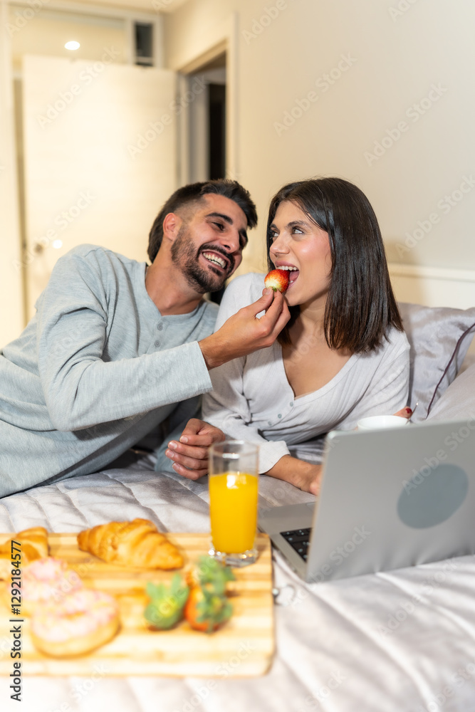 Happy couple enjoying breakfast in bed with laptop and strawberries Happy couple enjoying breakfast in bed with laptop and strawberries