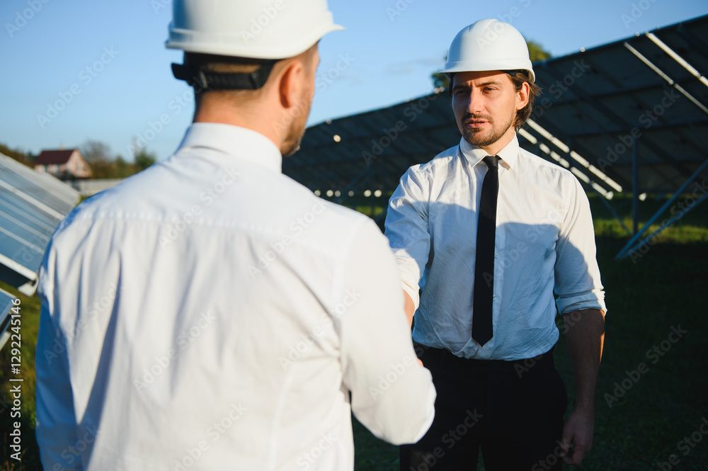 Two happy bearded workers in uniform talking and shaking hands near solar panel farm Two happy bearded workers in uniform talking and shaking hands near solar panel farm