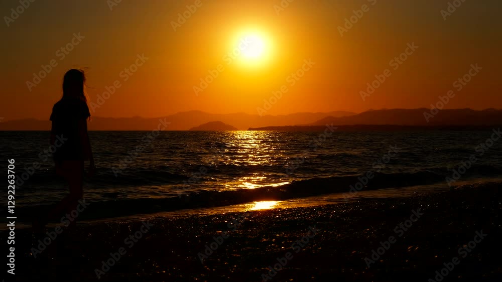 Girl walk on dusk shore against horizon. A young girl silhouette walk along the beach against orange horizon. A concept of sea relaxation during vacation time. Girl walk on dusk shore against horizon. A young girl silhouette walk along the beach against orange horizon. A concept of sea relaxation during vacation time.