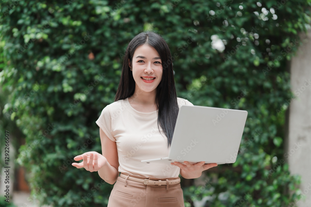 Professional Woman with Laptop: A stylish young woman with a bright smile, holding a laptop. She is standing near the backdrop of green foliage. The image portrays a blend of work, style. Professional Woman with Laptop: A stylish young woman with a bright smile, holding a laptop. She is standing near the backdrop of green foliage. The image portrays a blend of work, style.