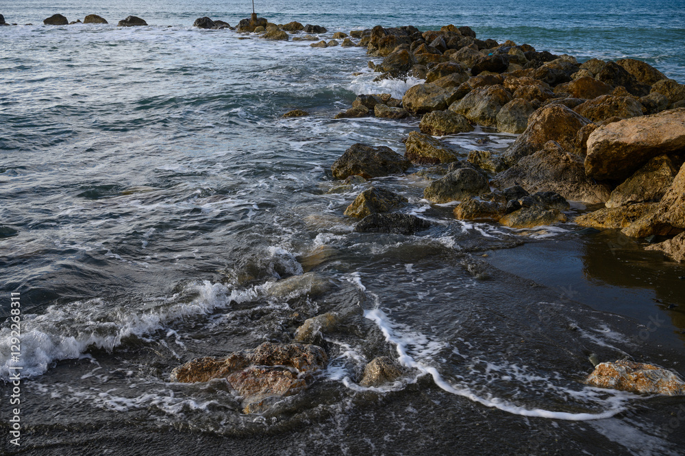 Waves gently lap against rocky shore at sunset with vibrant colors and serene atmosphere Waves gently lap against rocky shore at sunset with vibrant colors and serene atmosphere