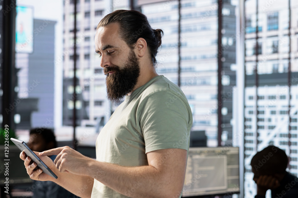 Startup employee walking in office, using tablet to do research for project with deadline approaching. Man using digital device in workspace, solving tasks during job shift, city backdrop Startup employee walking in office, using tablet to do research for project with deadline approaching. Man using digital device in workspace, solving tasks during job shift, city backdrop