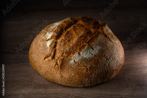 Billede på lærred Artisan bread loaf resting on wooden surface with warm light highlighting crust