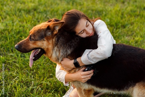 Veterinarian is hugging her german shepherd dog in a green meadow at sunset, showing love, care, and the strong bond between humans and animals