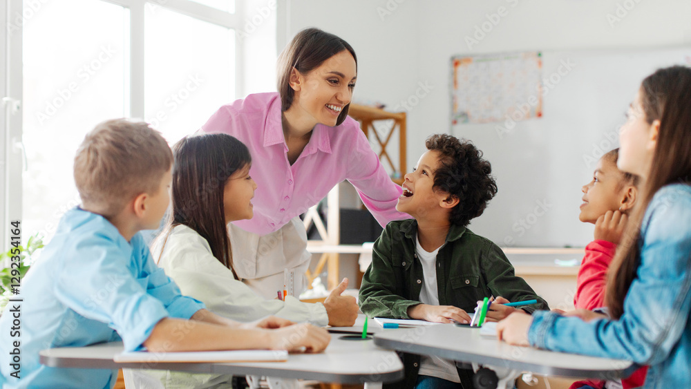 Cheerful teacher talking to kids, children sitting at desks in classroom and listening their teacher with interest, panorama Cheerful teacher talking to kids, children sitting at desks in classroom and listening their teacher with interest, panorama