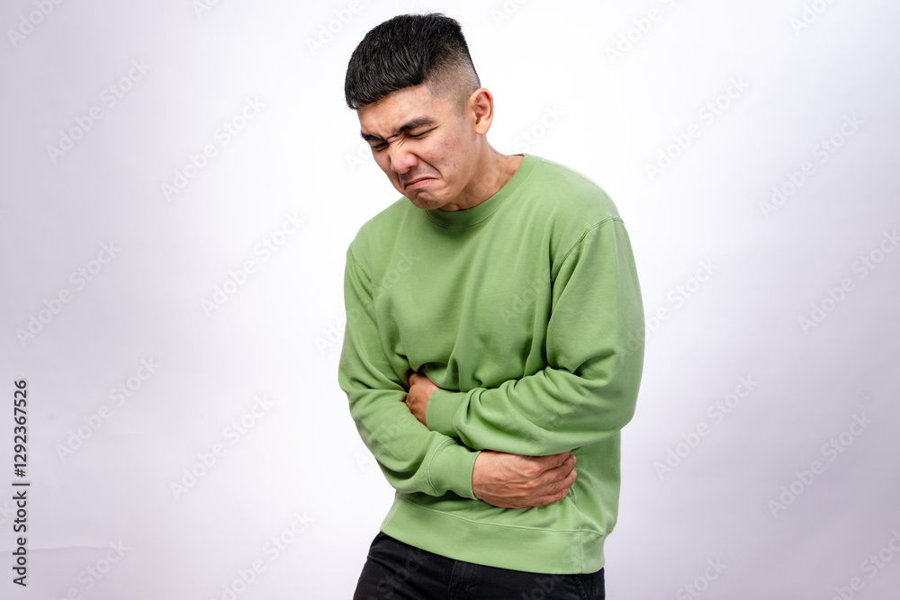 An Asian man in a green sweatshirt is grimacing in pain, holding his stomach and lower back. His facial expression suggests intense discomfort. The background is plain white An Asian man in a green sweatshirt is grimacing in pain, holding his stomach and lower back. His facial expression suggests intense discomfort. The background is plain white