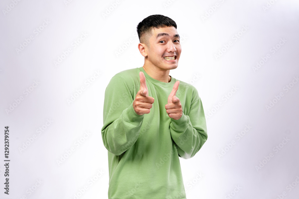A cheerful Asian man in a green sweatshirt smiles playfully while pointing both index fingers forward. He stands against a plain white background, conveying confidence, and a fun attitude A cheerful Asian man in a green sweatshirt smiles playfully while pointing both index fingers forward. He stands against a plain white background, conveying confidence, and a fun attitude