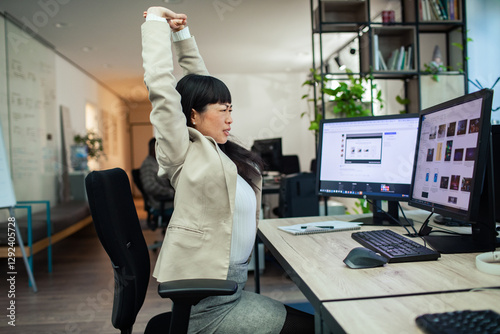 Asian businesswoman stretching at office desk while working on computer photo