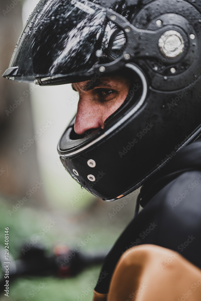 Fototapeta premium Hombre adulto en motocicleta negra por camino rodeado de arboles en día lluvioso