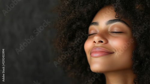 A woman with curly hair is capturing a peaceful moment with her eyes closed and a gentle smile. Her relaxed expression suggests a feeling of contentment and joy in a serene setting