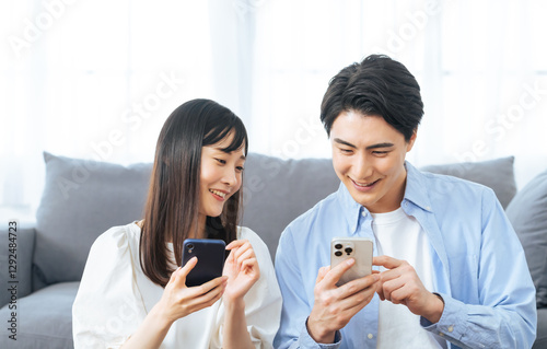 Obraz na płótnie スマホ、スマートフォン、アプリ、カップル、夫婦、マッチング、動画、検索、情報、キャンペーン、ポイント、クーポン、二人、女性、男性、日本人、リビングルーム、ソファー、室内、部屋探し、同棲、新居、新生活、調べる、リサーチ、相談、メール、SNS、明るい、笑顔、楽しい、嬉しい、セール、インターネット、オンライン、web、予約、テクノロジー、DX、デジタル、データ、IT、ライフスタイル、リラックス、カジュア