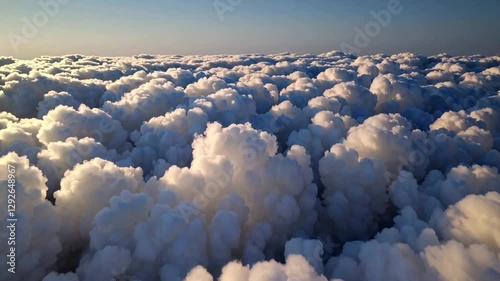 Aerial shot soaring through fluffy white clouds as soft early morning light pours through, casting long shadows. The clouds blend seamlessly with a soft blue sky.  Backgrounds
