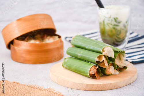 Serabi Solo on wooden plate. Traditional pancakes from Solo, Central Java. Made from flour dough baked on a special clay plate. Filled with various toppings then wrapped with banana leaf rolls	 photo