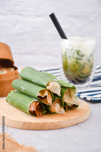 Serabi Solo on wooden plate. Traditional pancakes from Solo, Central Java. Made from flour dough baked on a special clay plate. Filled with various toppings then wrapped with banana leaf rolls	 photo