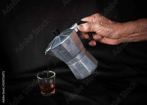 A man pouring coffee from moka pot into cup on table. 