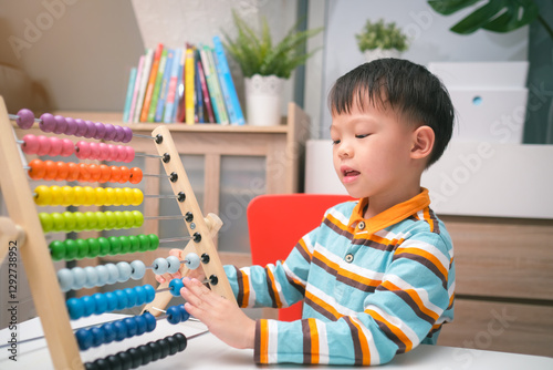 A focused 4-year-old Asian kindergarten boy practices using an abacus to learn math at home. Early childhood education, concentration, and cognitive development in a home learning environment