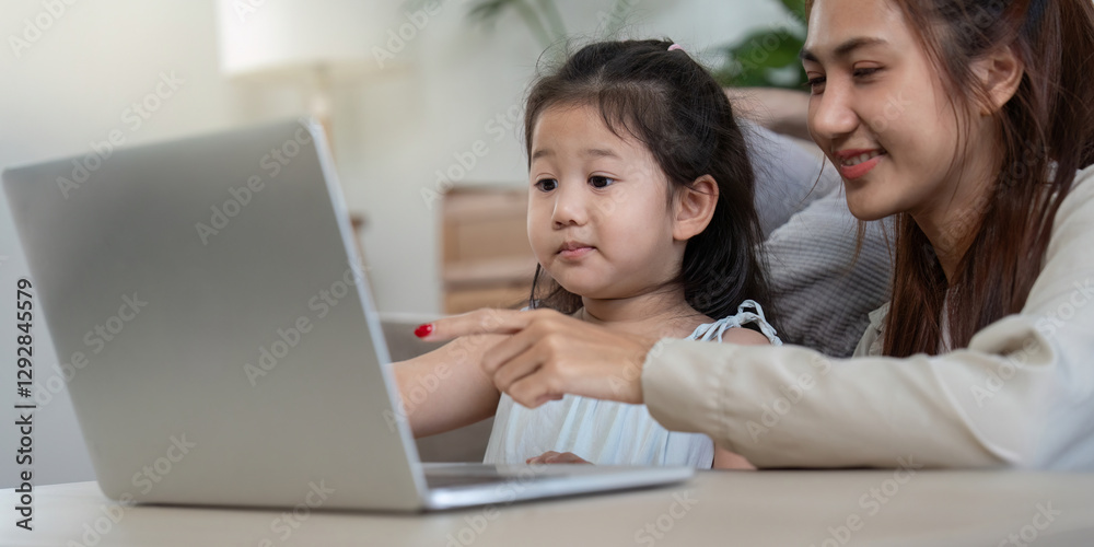 Mother and daughter engaged in a fun activity on a laptop, sharing smiles. Mother and daughter engaged in a fun activity on a laptop, sharing smiles.