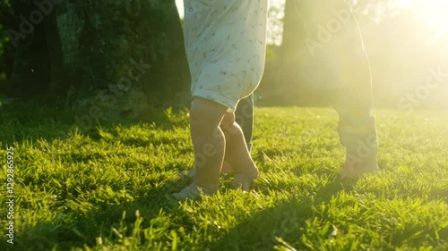 Walking children's bare feet on a green lawn close-up. Child  learns to take the first steps.  Baby learns to walk with the help of his mother on a green grass in the park. Real time 4k video.