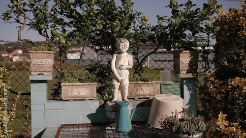 Stone pissing boy statue in a garden with potted plants and vintage elements