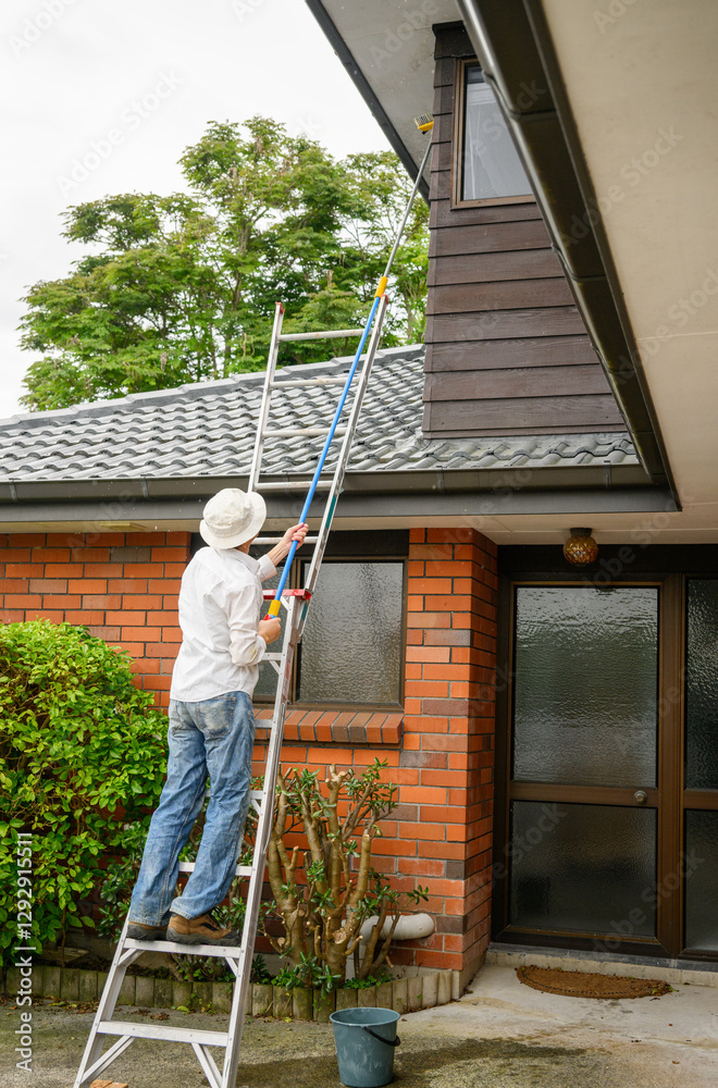 Man standing on the ladder and cleaning house with a long brush. Vertical format.
