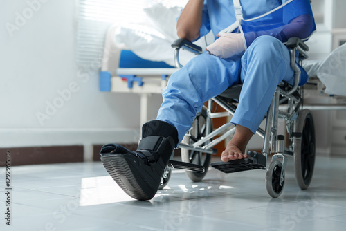Patient wearing arm sling and walking boot sitting in wheelchair in hospital room photo