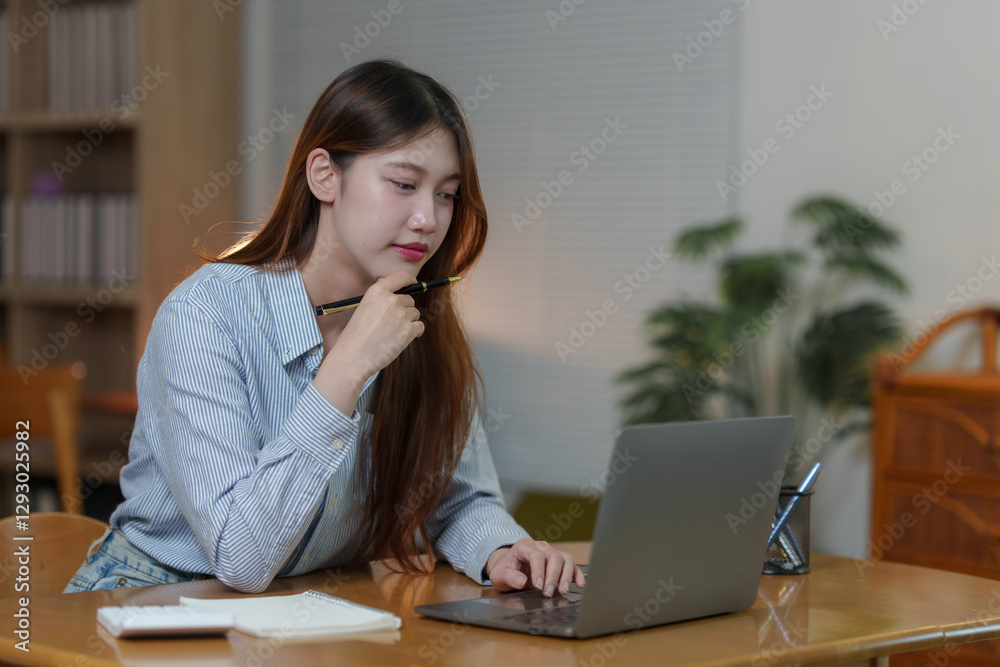 Young asian businesswoman working from home using laptop and thinking with pen in hand Young asian businesswoman working from home using laptop and thinking with pen in hand