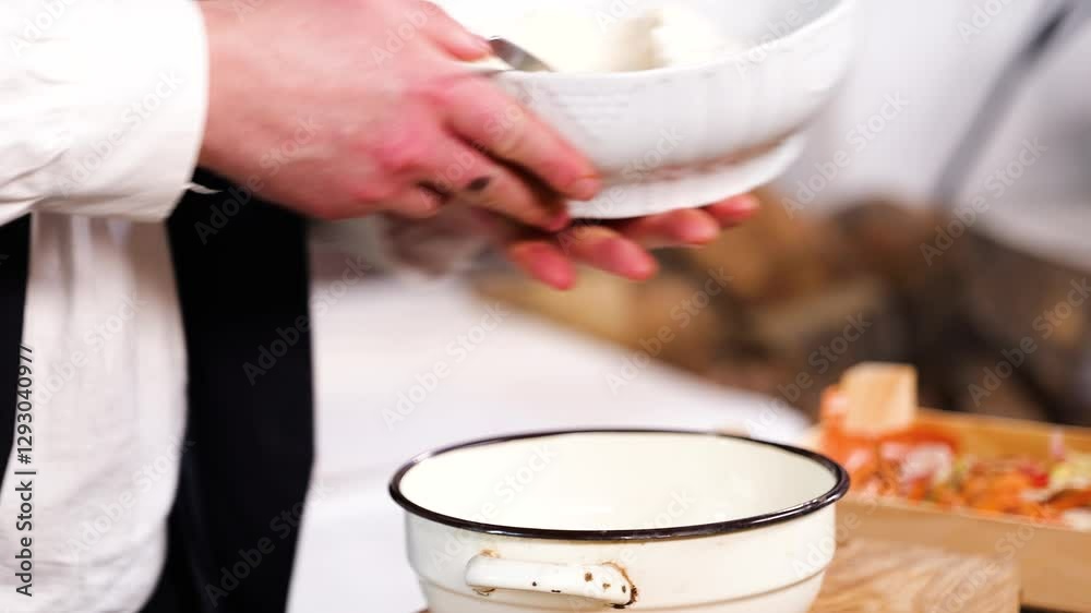 Medium shot of cook putting flour in a bowl with a spoon, cooking traditional hungarian food in an old kitchen with nomad ways, handheld Medium shot of cook putting flour in a bowl with a spoon, cooking traditional hungarian food in an old kitchen with nomad ways, handheld
