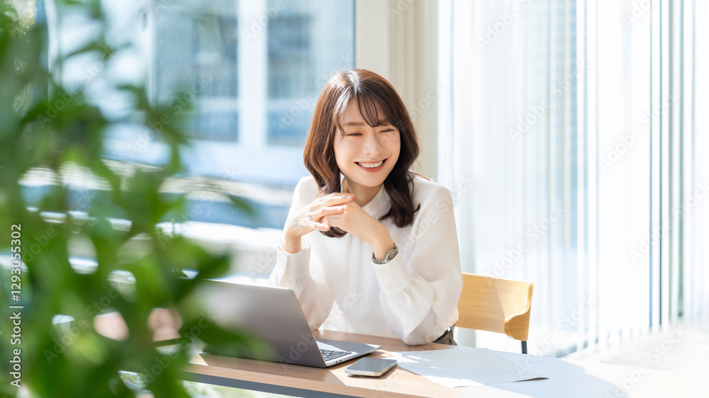 Fototapeta premium 春の光が差し込むオフィスでデスクワークをする笑顔の女性・ビジネスウーマン