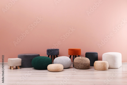 Different stylish poufs and ottomans near pink wall, space for text