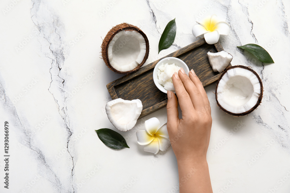Fototapeta premium Female hand, wooden tray, flowers and bowl with natural coconut oil on marble background