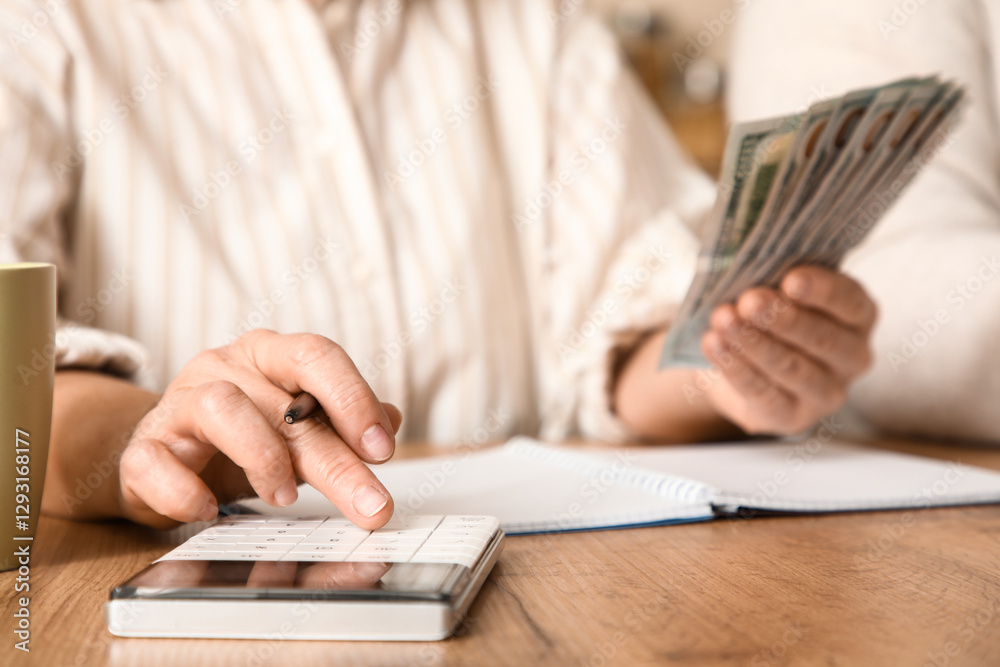 Fototapeta premium Senior woman with money calculating utility bills at table in kitchen, closeup