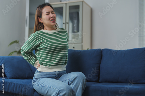 Free Download Young woman suffering from back pain while sitting on sofa at home - GFXLoad