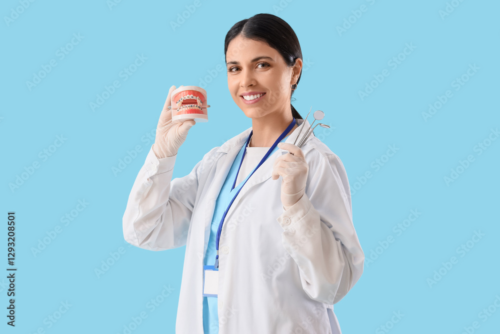Female dentist holding jaw model with braces and tools on blue background Female dentist holding jaw model with braces and tools on blue background