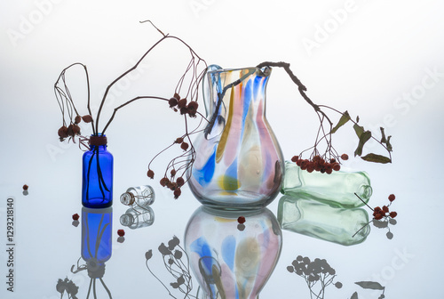 Glass jug with dry rowan branches with dried berries on a light background. Reflection in glass.