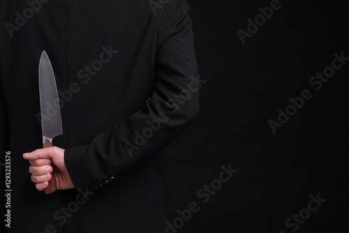 Businessman holding knife behind his back on black background, closeup. Space for text