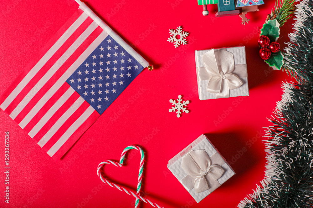Fototapeta premium A Boxing Day preparation flat lay featuring a U.S. flag, white gift boxes, candy canes shaped like a heart, snowflake decorations, holly, and Christmas greenery on a vibrant red background.