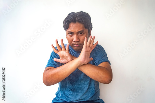 A man in a blue shirt is making a prohibitive gesture with crossed arms and open hands against a plain white background. This image is useful for illustrating concepts of refusal or denial